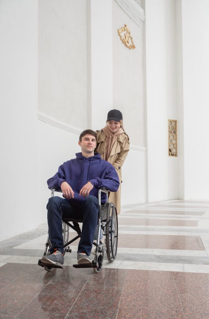 Crafting Captivating Headlines: Your awesome post title goes here Caucasian woman assists a man in a wheelchair in a bright hallway, signifying care and companionship.